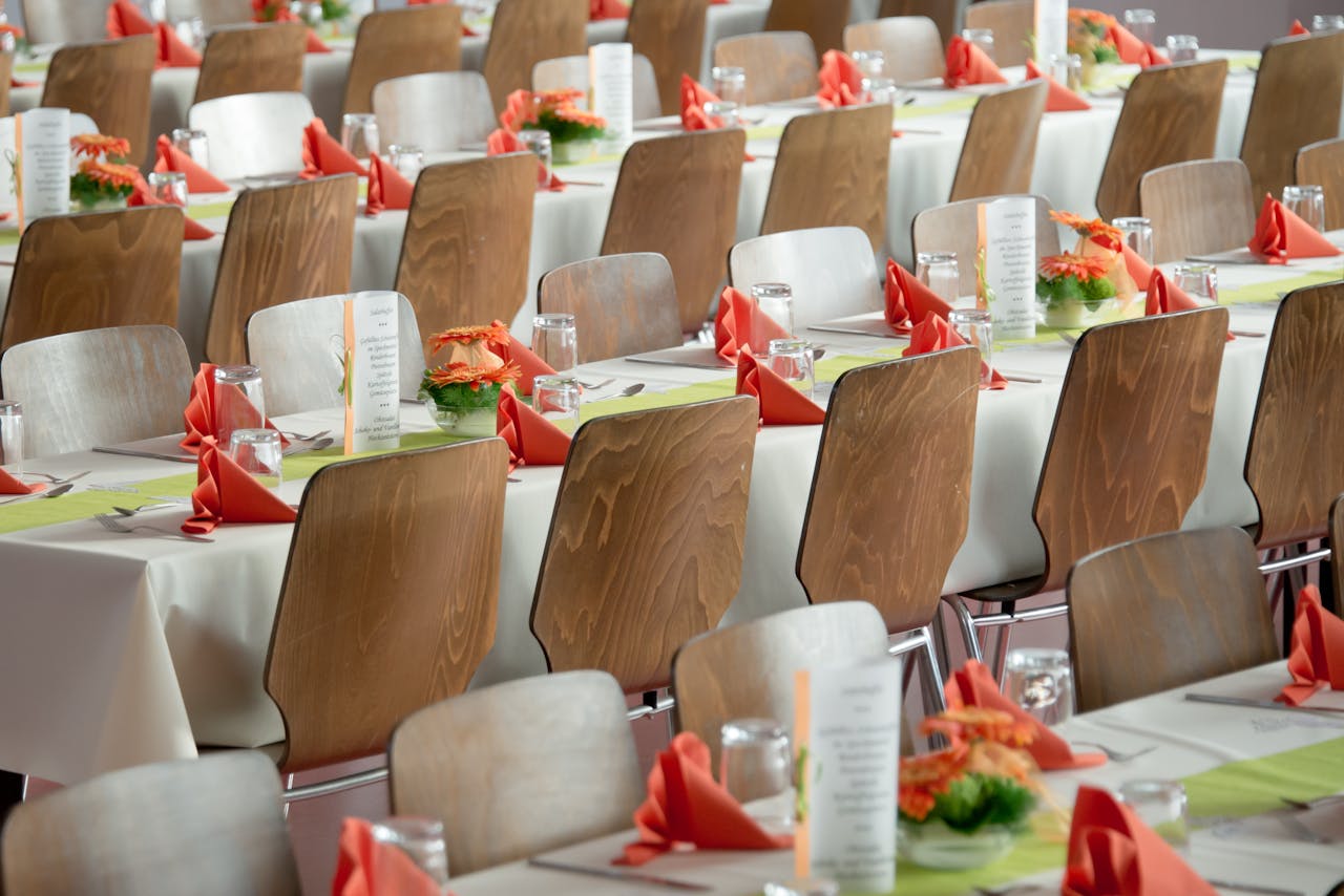 heros-img Beautifully arranged tables with wooden chairs for a formal event, adorned with orange flowers.